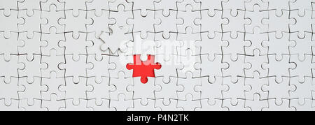 The texture of a white jigsaw puzzle in an assembled state with one missing element forming a red space . Stock Photo