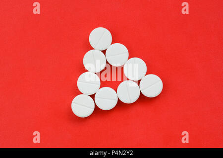 Several white tablets lie on a bright red background in the form of an ...