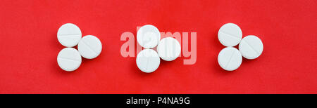 Several white tablets lie on a bright red background in the form of three triangular arrows. Background image on medicine and pharmaceutical topics . Stock Photo