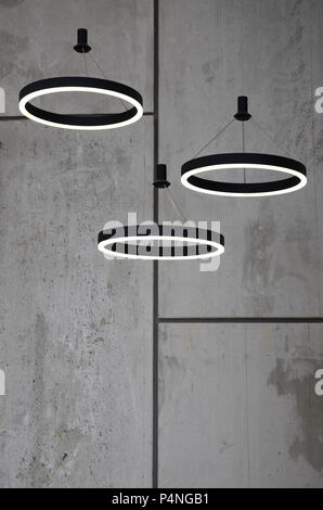 Unusual light sources hang on the background of a marble wall. Lamps in the form of a luminous ring . Stock Photo