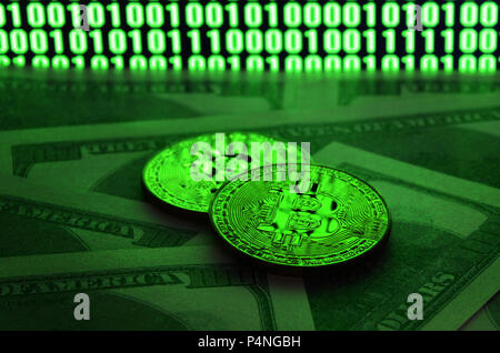 Two bitcoins lies on a pile of dollar bills on the background of a monitor depicting a binary code of bright green zeros and one units on a black back Stock Photo