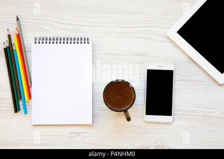 Workplace with smart phone, notebook, color pencils, tablet and latte on white wooden background. From above. Stock Photo