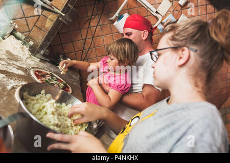 Naples, Italy - August 9, 2015: Preparing Classic Pizza Margherita. Chef with children add grated parmesan cheese Stock Photo