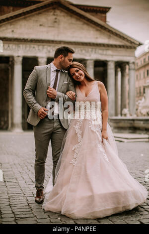 Young attractive newly married couple walking and posing in Rome with beautiful and ancient architecture on the background on their wedding day Stock Photo
