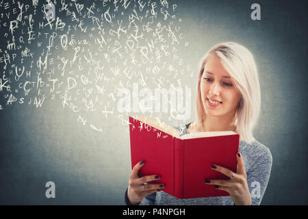 Beautiful blonde girl read and flying alphabet letters escape from the red book. The magic of lecture. Young school teacher studying, educational and  Stock Photo