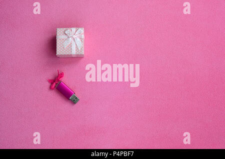 Brilliant pink usb memory card with a pink bow lies next to a small gift box in pink with a small bow on a blanket of soft and furry light pink fleece Stock Photo