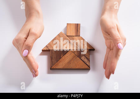 Close-up Of A Woman's Hand Protecting House Made Of Wooden Tangram Puzzle Over Desk Stock Photo