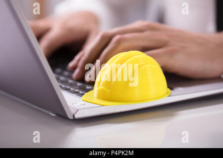 Close-up Of A Yellow Hardhat On Laptop Keypad Over Desk Stock Photo