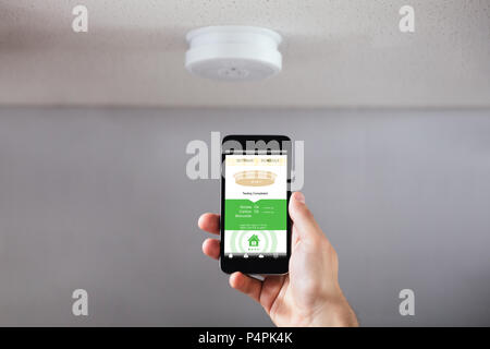 Close-up Of A Person's Hand Operating Smoke Detector With Mobile Phone Stock Photo