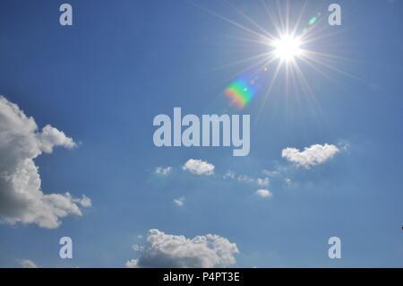 Cloudscape with a blue sky and the sun shining with rainbow reflections Stock Photo