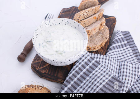 Yoghurt with cucumber. Fresh dip of famous Greek taziki with cucumber. fresh bread, towel and white background. Copy space Stock Photo
