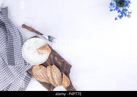 Yoghurt with cucumber. Fresh dip of famous Greek taziki with cucumber. fresh bread, towel and white background. Copy space. Stock Photo