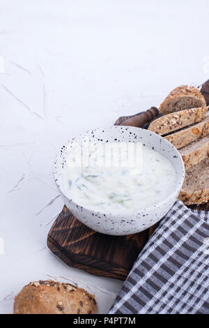 Yoghurt with cucumber. Fresh dip of famous Greek taziki with cucumber. fresh bread, towel and white background. Copy space Stock Photo