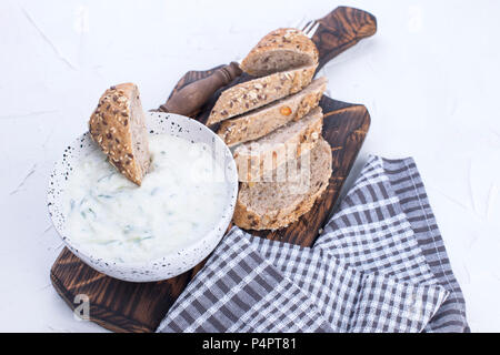 Yoghurt with cucumber. Fresh dip of famous Greek taziki with cucumber. fresh bread, towel and white background. Copy space. Stock Photo