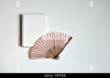 Pink fan and notebook in the middle on white background, flat lay, copy space, minimalist style Stock Photo