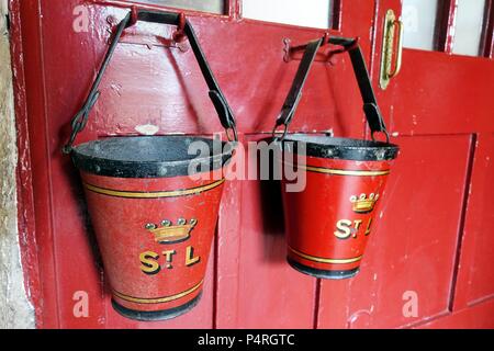 Marazion, Cornwall, UK - April 13 2018: Two old fashioned vintage antique fire buckets hanging on a red door Stock Photo