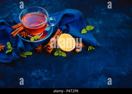 Black tea glass teacup, linen napkin, lemon slices, cinnamon, anise stars and mint leaves on a dark background. Dark food photography header with copy Stock Photo