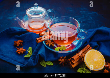 Black tea glass teacup, linen napkin, lemon slices, cinnamon, anise stars and mint leaves on a dark background. Dark food photography header with copy Stock Photo