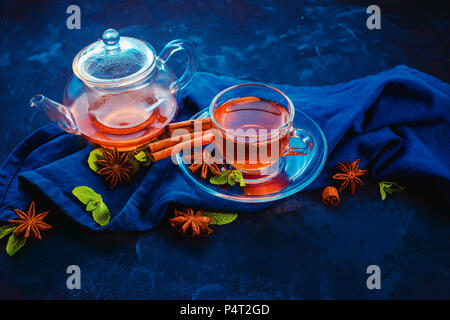 Black tea in a glass cup and a tiny teapot with lemon slices and mint leaves on a dark background. Vibrant colors hot drink header with copy space. Stock Photo