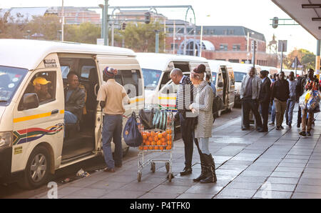 Pretoria, South Africa, June 7 - 2018: Commuters at minibus taxi rank looking at oranges on sale. Stock Photo