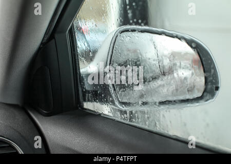 View from inside the car, looking at side mirror, wet from water and soap when being washed in carwash. Stock Photo