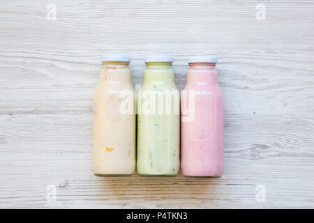 Fruit smoothies of different colors in glass jars on white wooden background. Top view, from above. Stock Photo