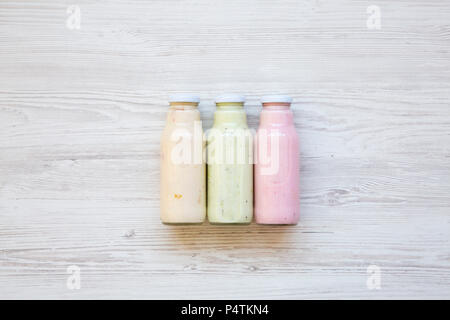 Fruit smoothies of different colors in glass jars on white wooden background. Top view, from above. Stock Photo