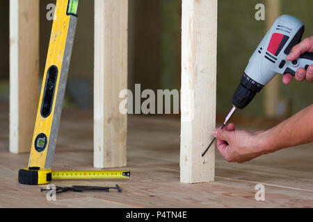 Close-up of worker's hands with screwdriver on background of professional tools and wooden frame for future wall in unfinished attic room under recons Stock Photo