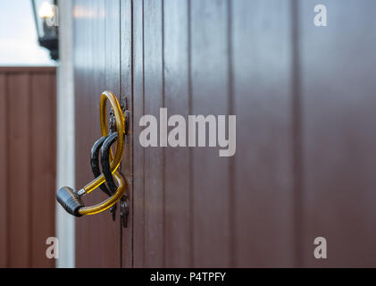 Shallow focus of a generic steel-wire bicycle antitheft device seen looped through the handles of a double door garage. Stock Photo