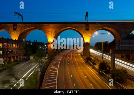 The M60 motorway runs below the Stockport railway viaduct as a train passes at night. Stock Photo