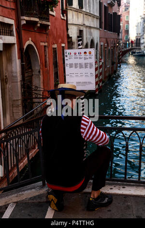 Behind a Venetian gondolier as he kneels and posts his sign to a small canal bridge, Venice, Italy Stock Photo