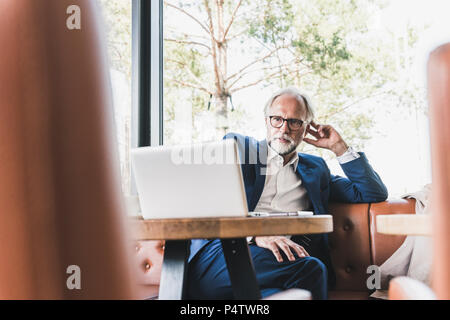 Mature businessman sitting at table in a cafe using laptop Stock Photo