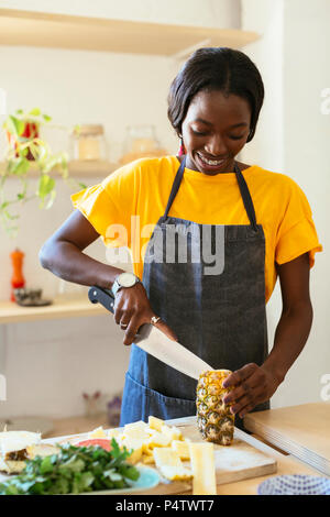 Smiling woman cutting pineapple in kitchen Stock Photo
