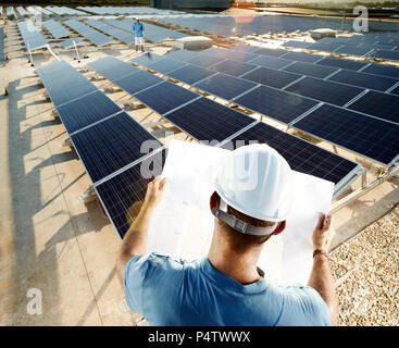 Back view of engineer looking at plan in front of solar plant Stock Photo