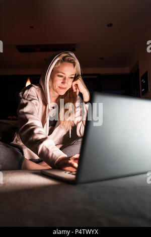 Smiling woman sitting on couch at home looking at laptop Stock Photo