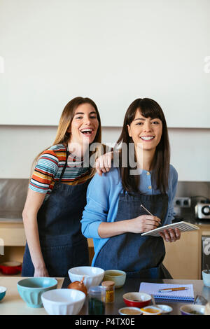 Portrait of two happy women with notebook in kitchen Stock Photo