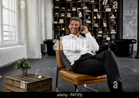 Smiling mature man using smartphone in loft Stock Photo
