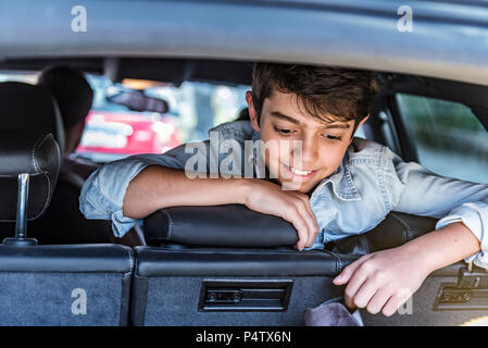 Smiling boy in car looking in boot Stock Photo