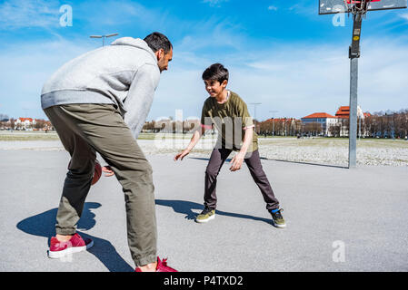 Father and son playing basketball on court outdoors Stock Photo