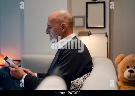 Senior man sitting on couch, reading book Stock Photo