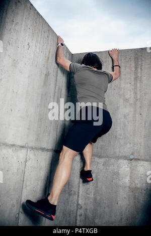 Athlete climbing up concrete wall outdoors Stock Photo