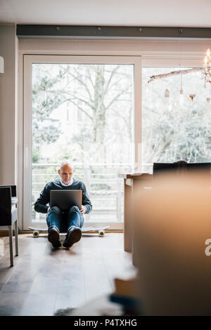 Senior man sitting on ground, using laptop Stock Photo