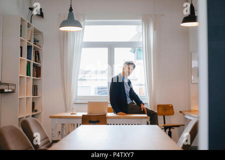 Portrait of smiling man sitting on table with laptop Stock Photo