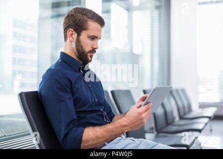 Young businessman sitting in waiting area using tablet Stock Photo