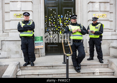 London, UK. 23 June 2018.Anti-Brexit march and rally for a People's Vote in Central London. Policemen guard the front door of the Cabinet Office after it had been defaced with stickers by protesters. Stock Photo