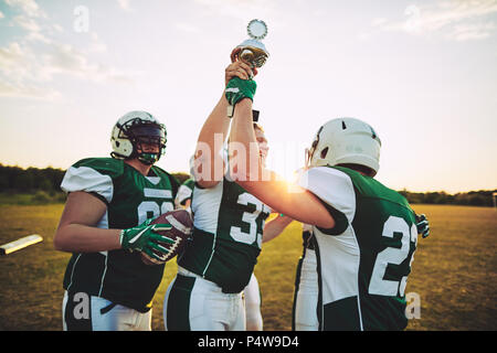 Team of young American football players celebrating victory and raising a championship trophy together after a game Stock Photo