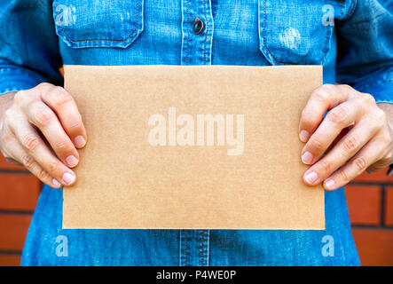 Woman hands holding piece of cardboard against brick wall background. Stock Photo