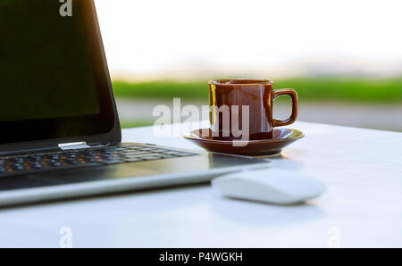 Notebook laptop with hot coffee on Mix of office supplies and gadgets wood table. Stock Photo