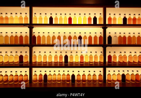 Unmarked glass whiskey bottles displayed on backlit shelves Stock Photo