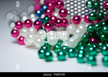 Macro abstract background featuring multi colored Mardi Gras bead necklaces randomly arranged on a white surface Stock Photo